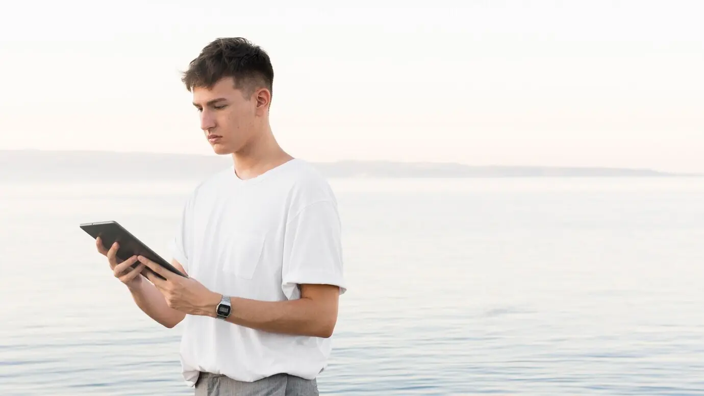Seitenansicht eines Mannes am Strand, der ein Tablet mit Platz für Text hält.